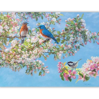 Two bluebirds and a chickadee perched on flowering branches against a blue sky.
