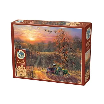 Jigsaw puzzle box with a scenic design of a sunset over a field and tractor, featuring the Cobbles Hill brand.